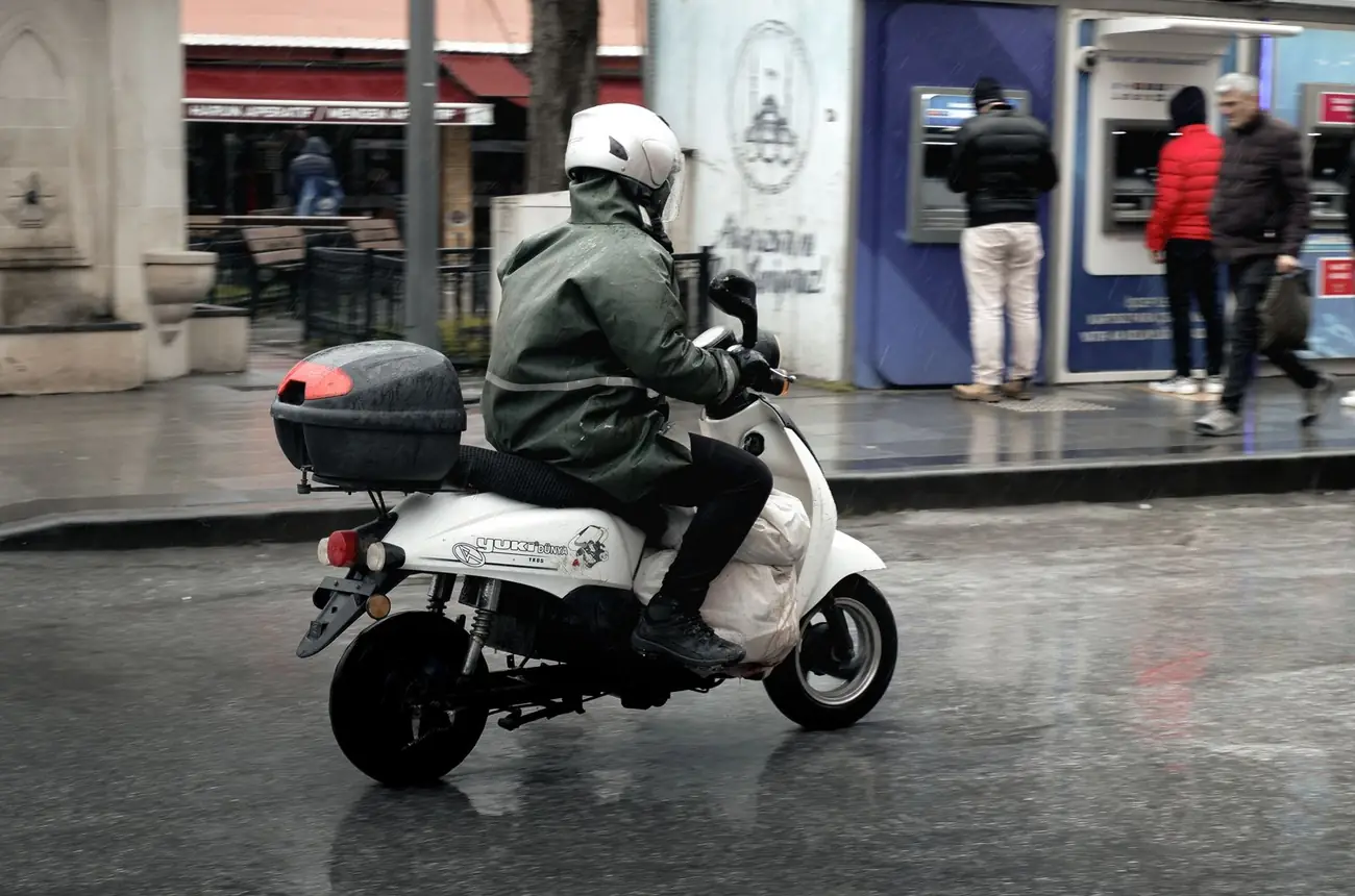 Scooter 125 avec top case qui roule sur une chaussée mouillée en ville