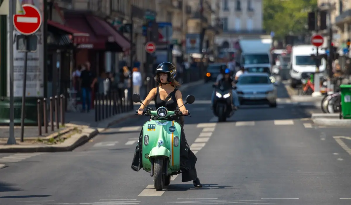 Femme casquée sur un scooter vert dans une rue de Paris